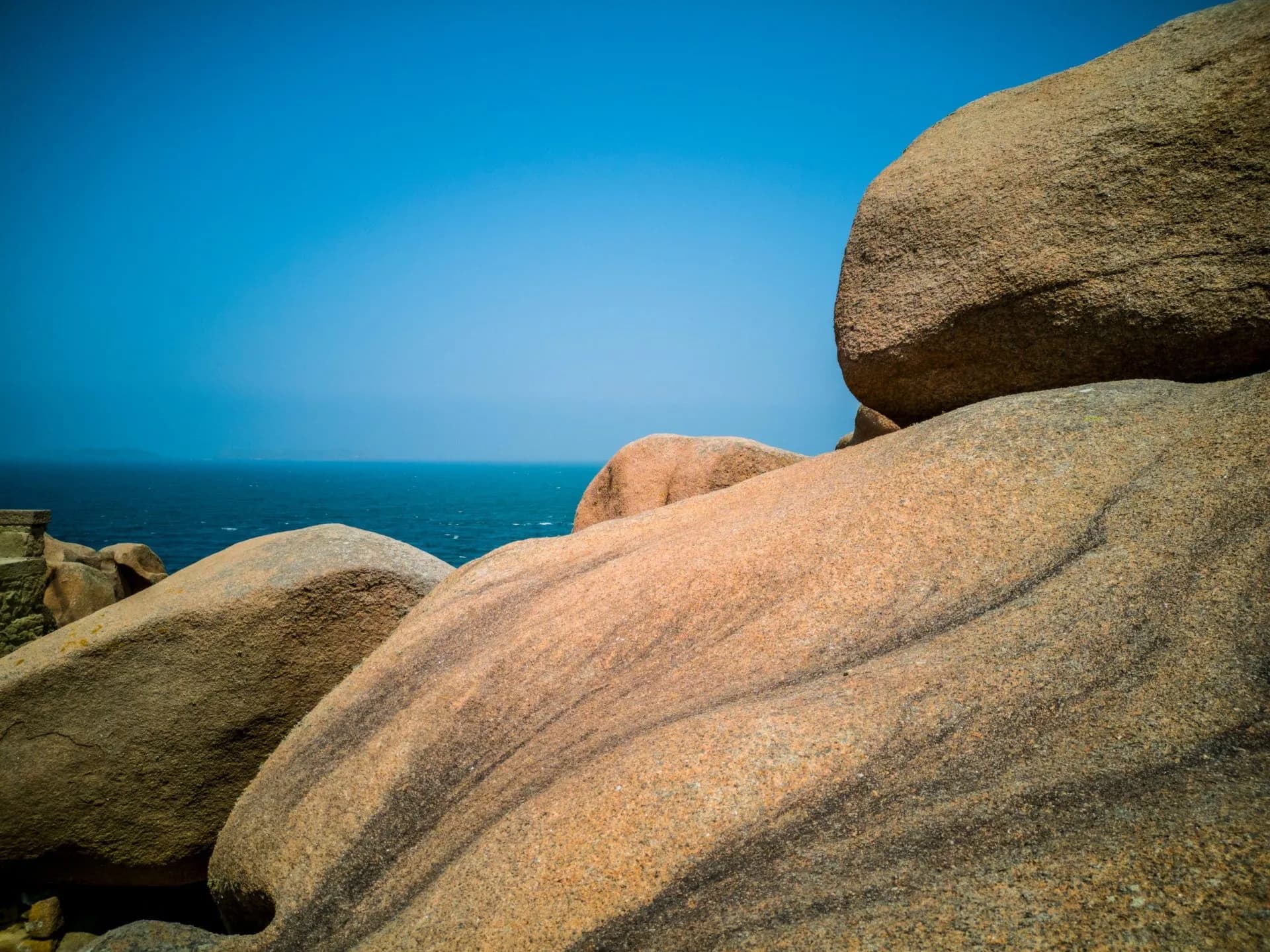 Pink granite boulders overlooking the deep blue sea under a clear sky, Côte de Granit Rose