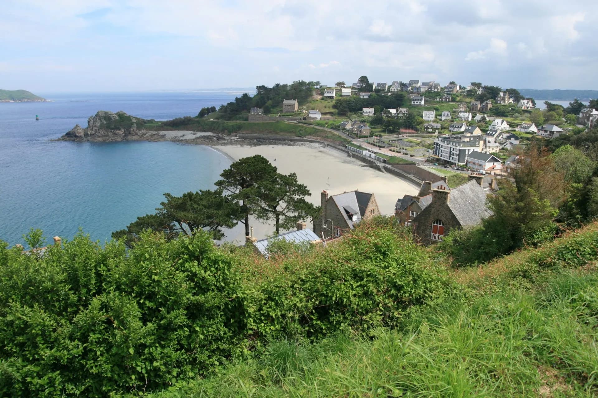 Coastal village with houses on a hillside overlooking a sandy beach and blue sea in Guirec.