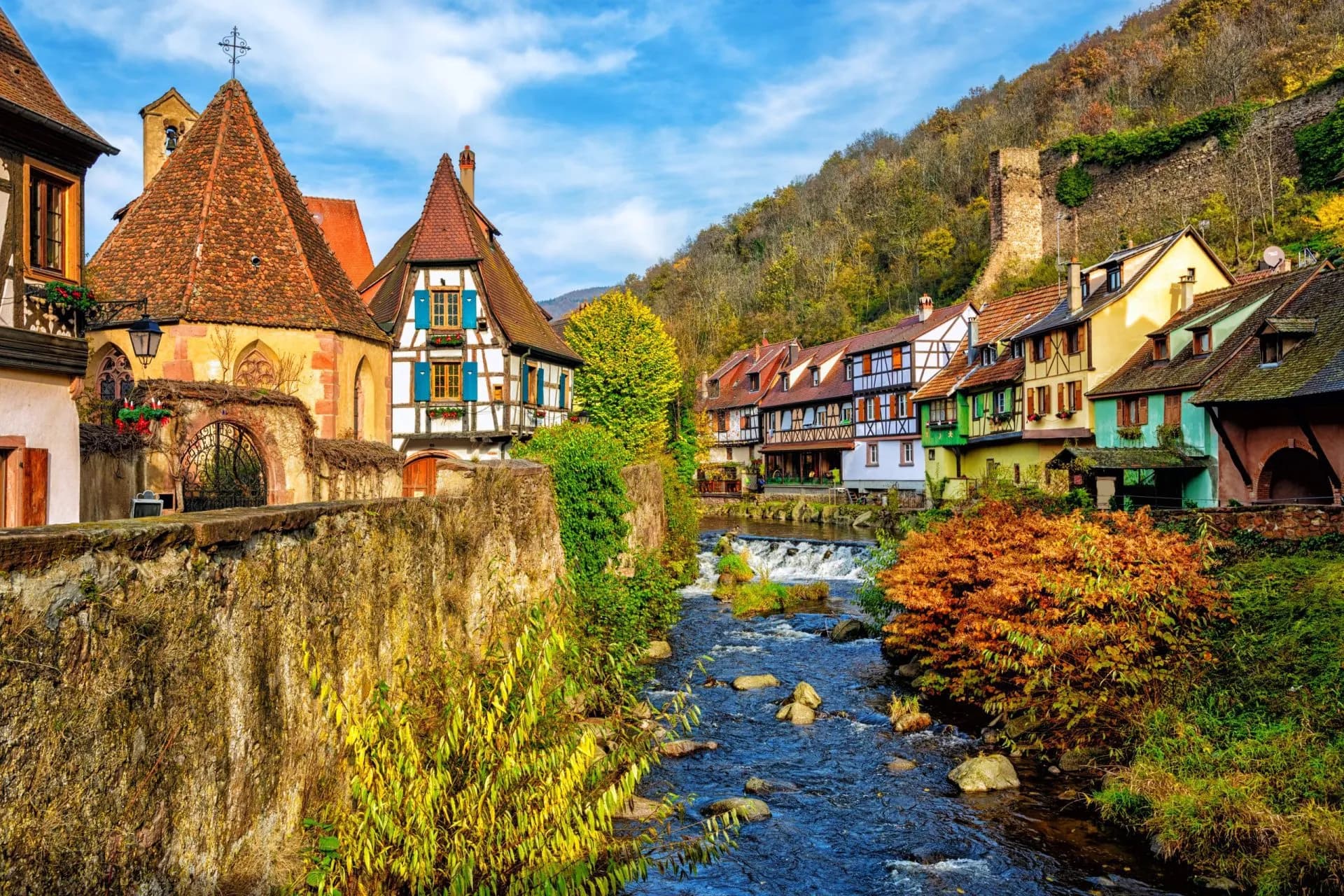 Half-timbered houses along a stream with autumn foliage in Kaysersberg.