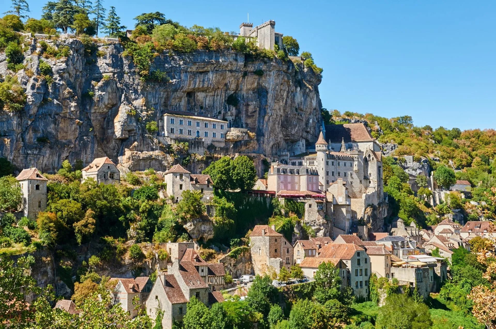 Rocamadour village clinging to a steep limestone cliff under a clear blue sky.