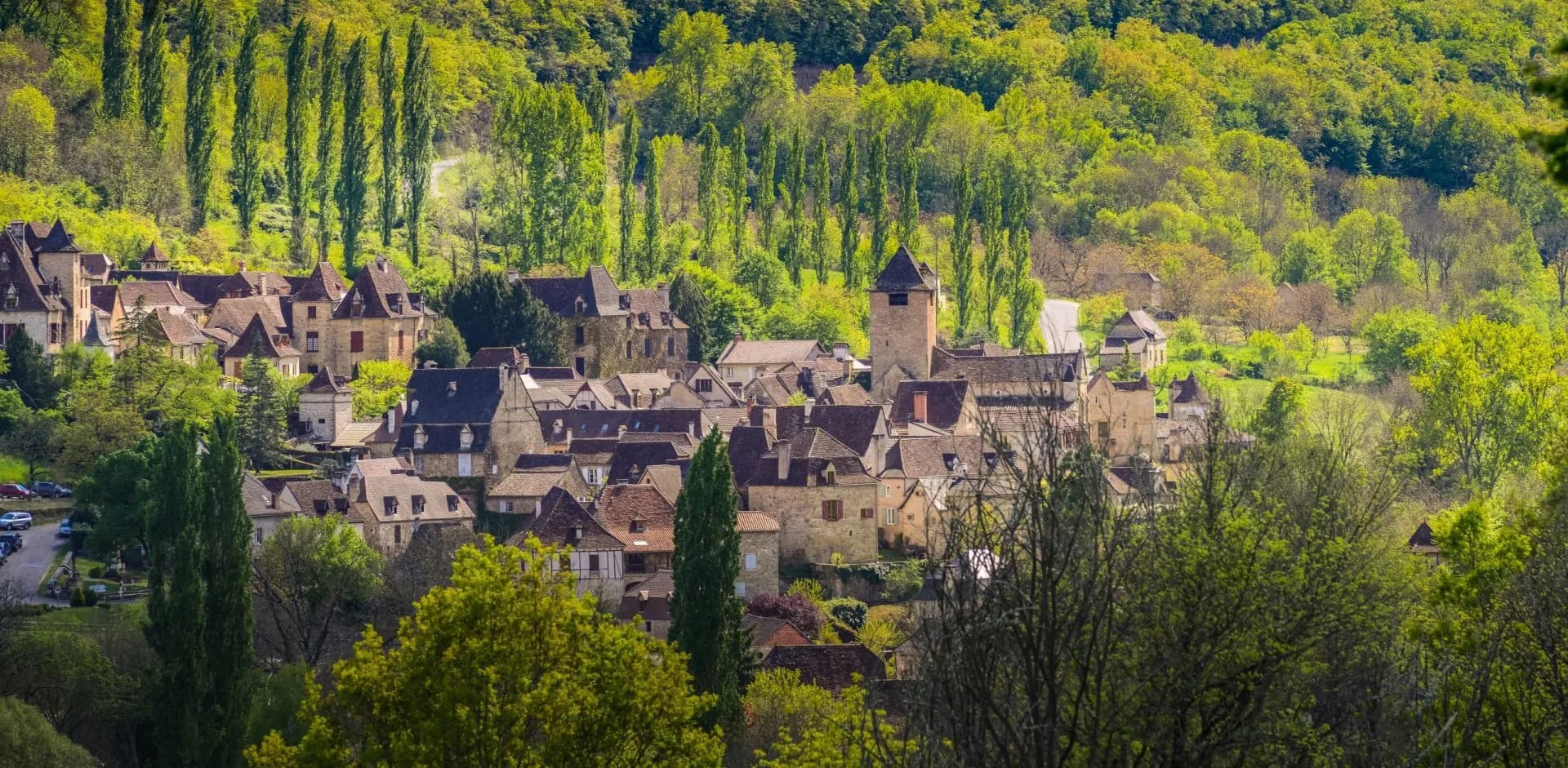 Historic European village nestled in lush green hillsides with stone buildings and terracotta roofs.