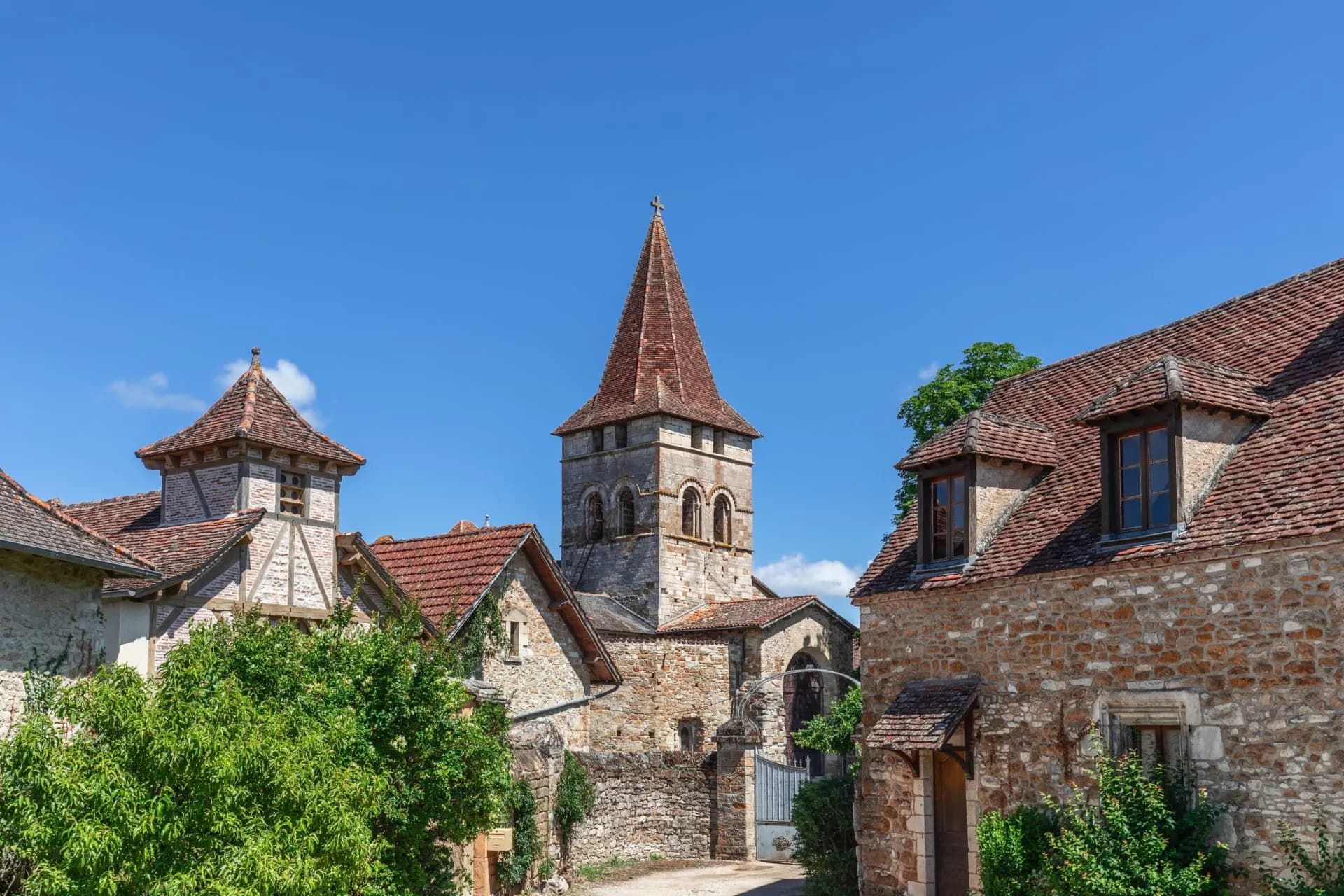 Stone church tower with terracotta roof surrounded by traditional stone houses under a clear blue sky.