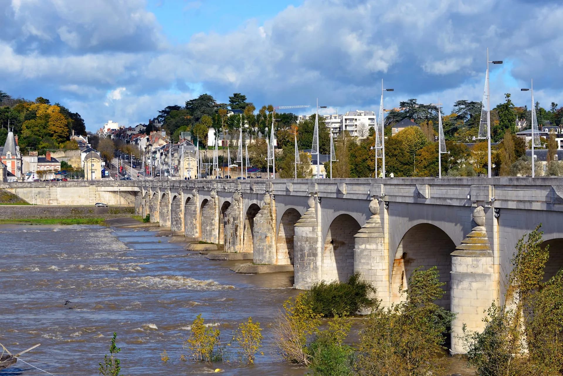 Stone arch bridge over the Loire River with Tours city skyline under cloudy skies.
