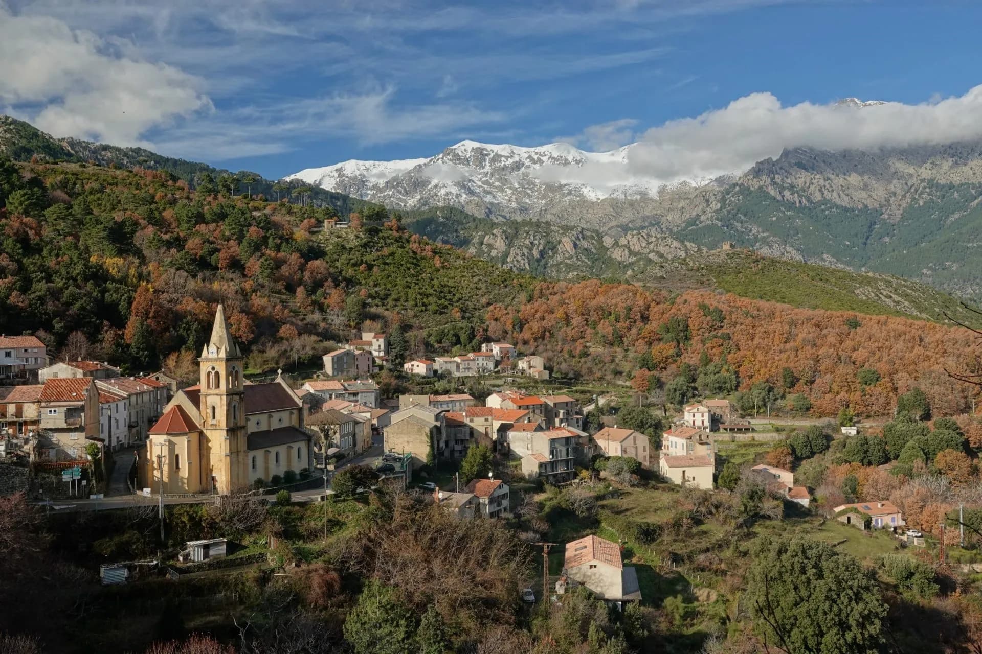 Village with church nestled in hillsides below snow-capped mountains, likely Vivario.