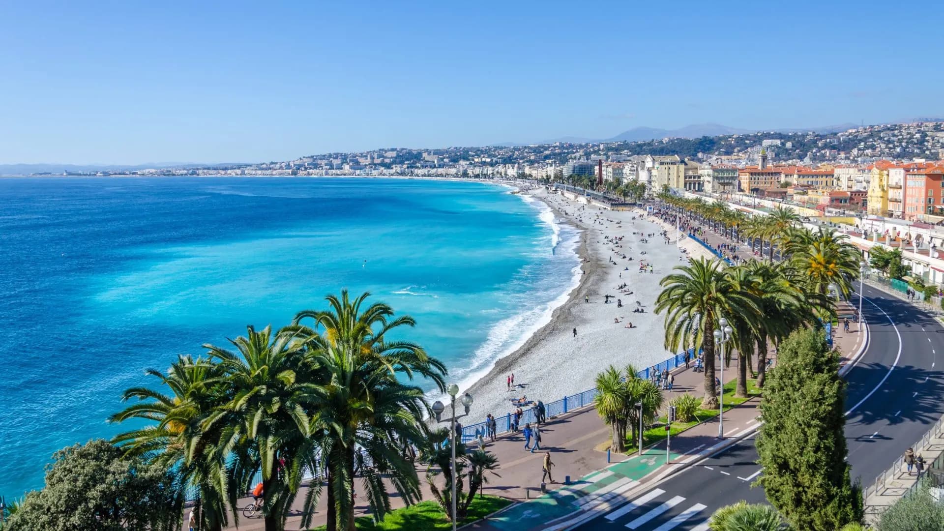 Bay of Angels in Nice with turquoise sea, pebble beach, palm trees, and coastal promenade.