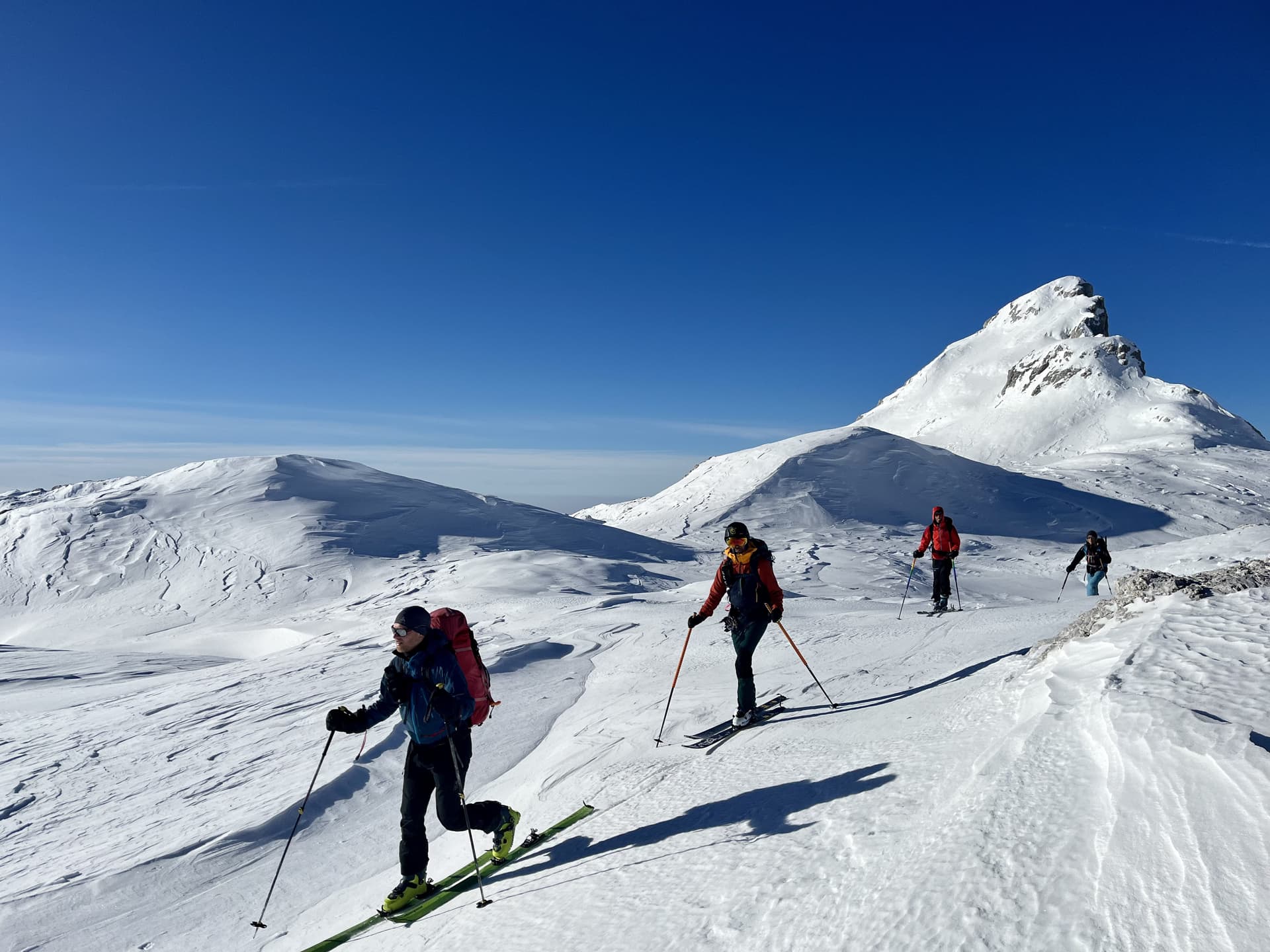 Ski touring near Triglav with people ascending snow-covered alpine mountains under a clear blue sky.