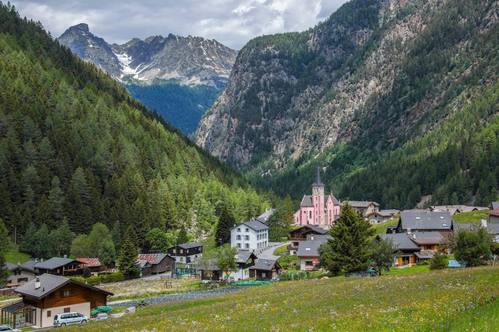 Alpine village of Trient nestled in a valley with a pink church and forested mountains.