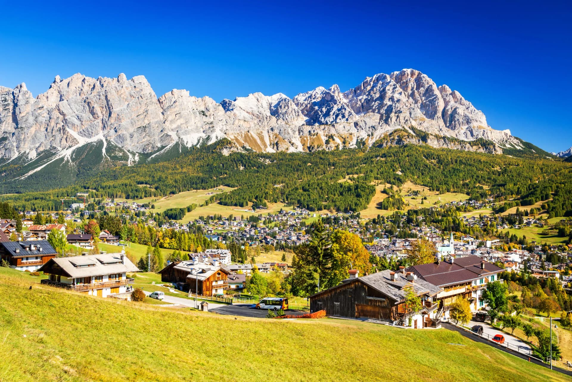 Alpine village nestled below rugged, sunlit mountains under a clear blue sky in Cortina d'Ampezzo.