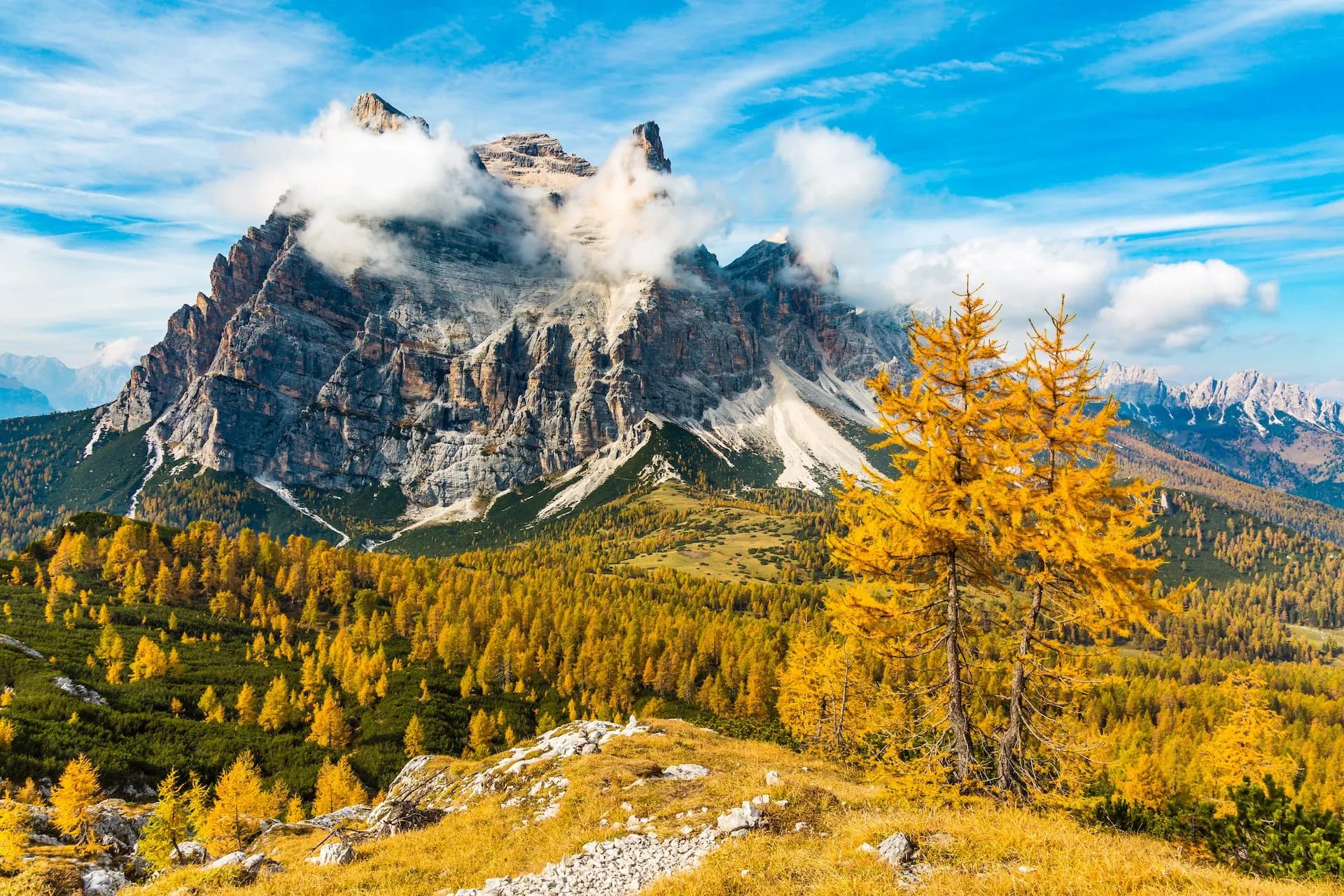 Monte Pelmo peak with clouds, autumn yellow larch trees, and blue sky in the Dolomites.