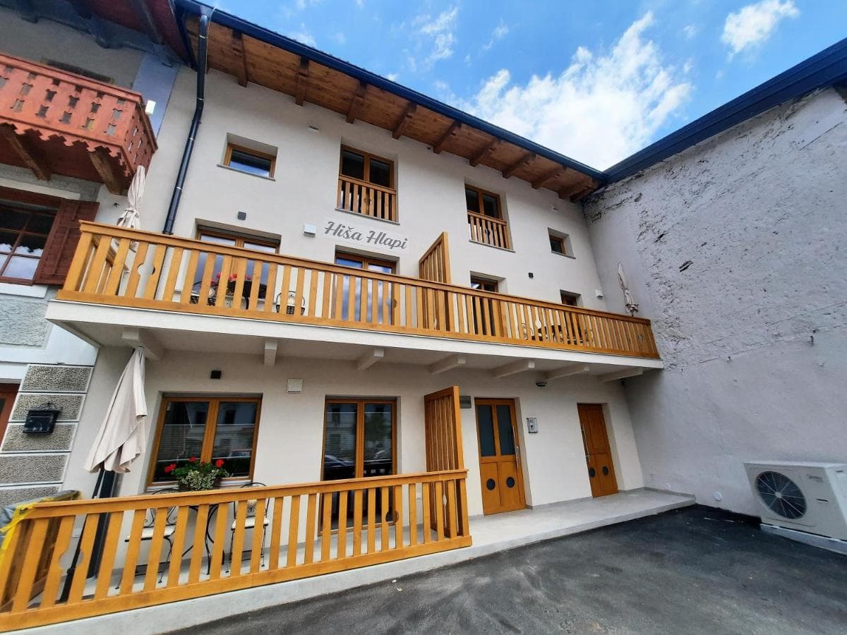 Apartments Hiša Hlapi building with wooden balconies under a blue sky with clouds