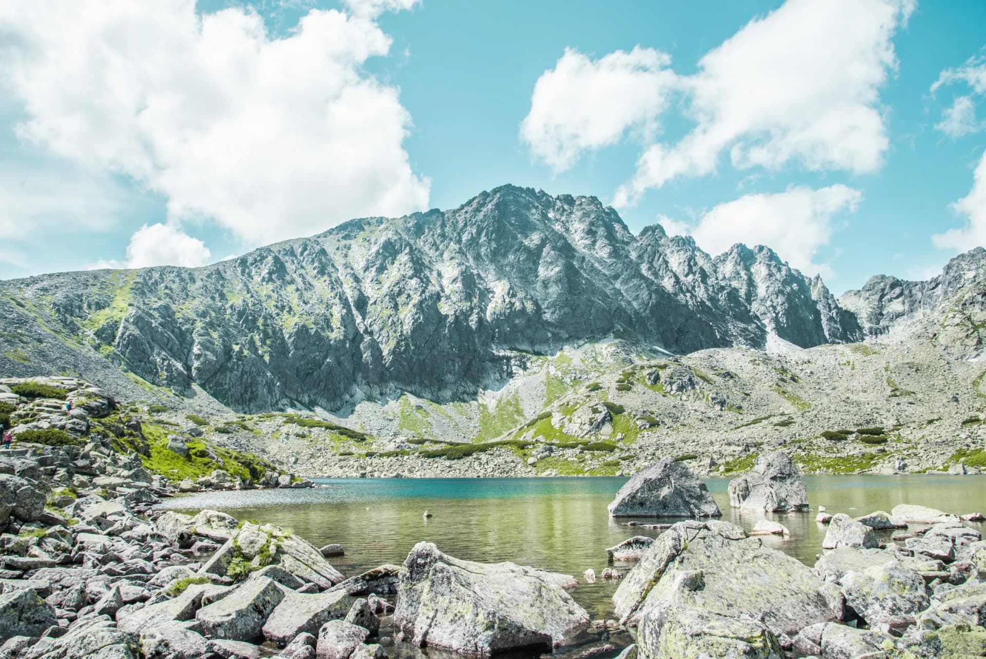 Rocky shore of Batizovske Pleso lake with a large mountain under a bright sky in the Tatras.