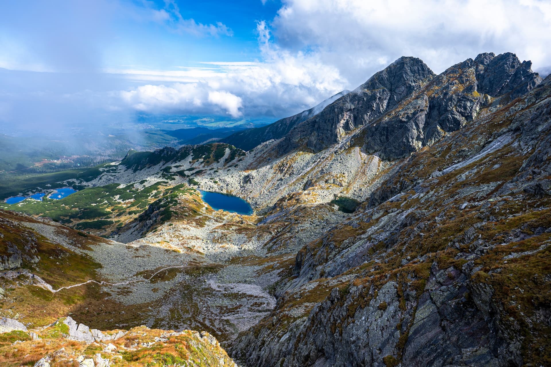 Hiking trail winding past glacial lakes below rugged, rocky peaks of Mount Kościelec, Tatras.