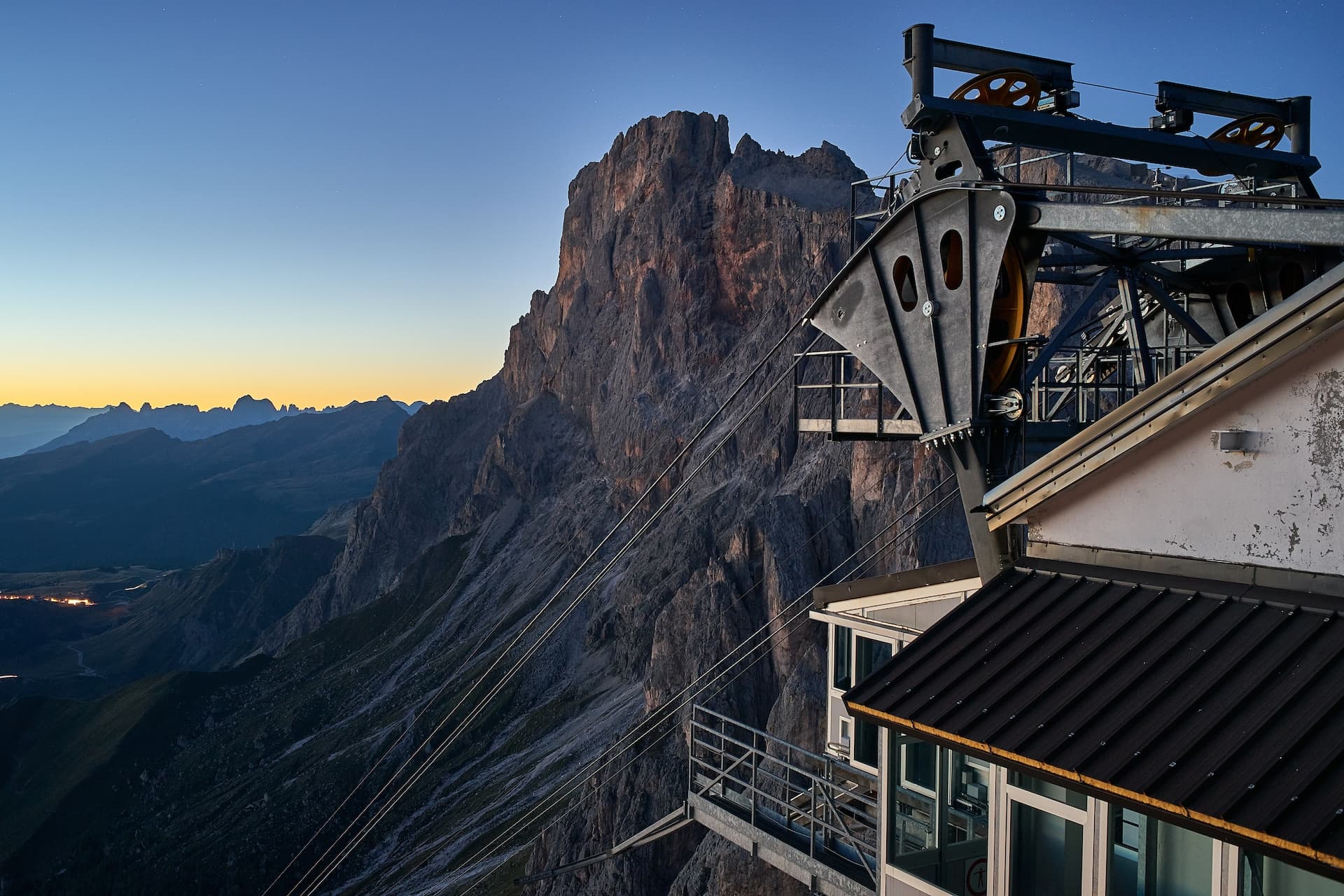 Gondola ride station mechanism against massive rocky mountain at twilight, Cima Rosetta.