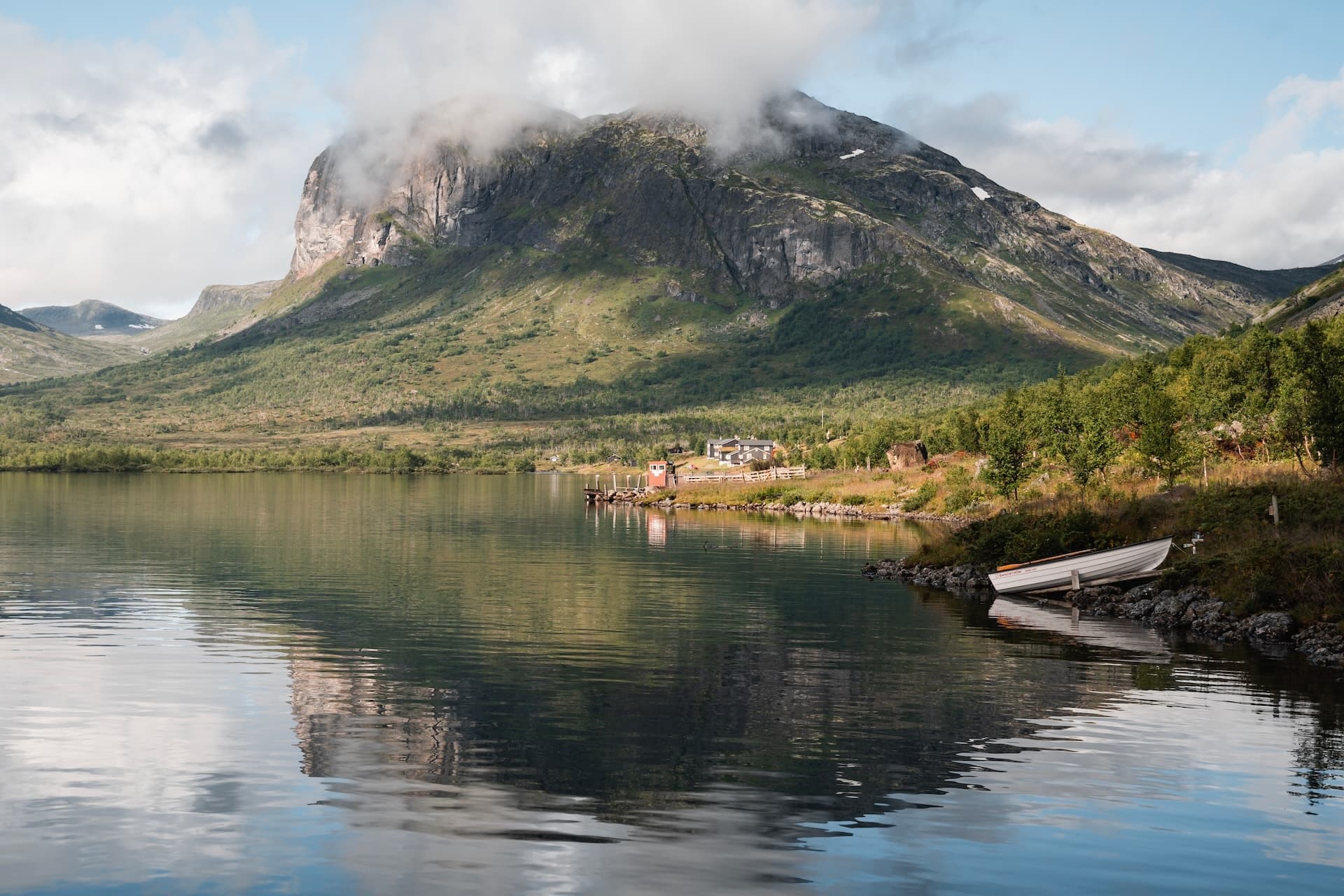 Small white boat pulled ashore on Gjende lake with mountain reflection.