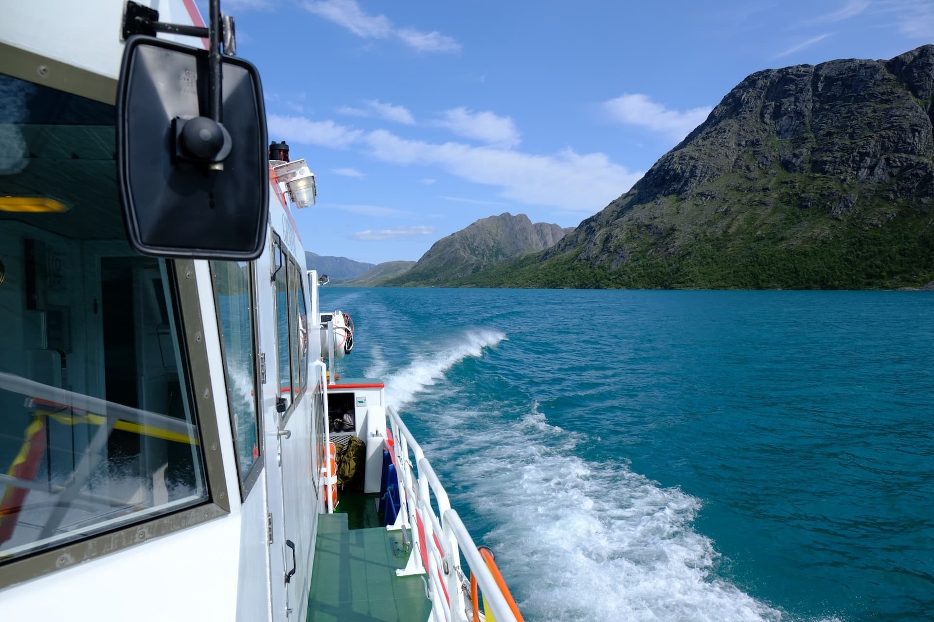 Ferry boat wake on turquoise water past steep green mountains on Gjende lake.