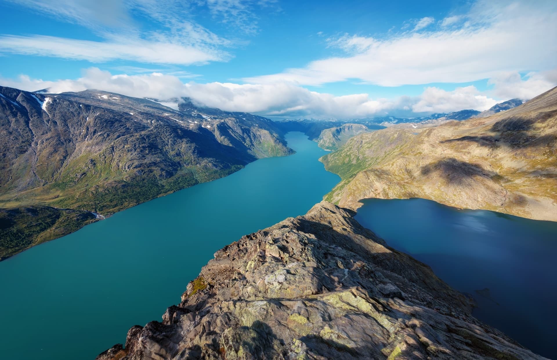 Aerial view of Besseggen Ridge overlooking turquoise Gjende lake and mountains under blue sky.