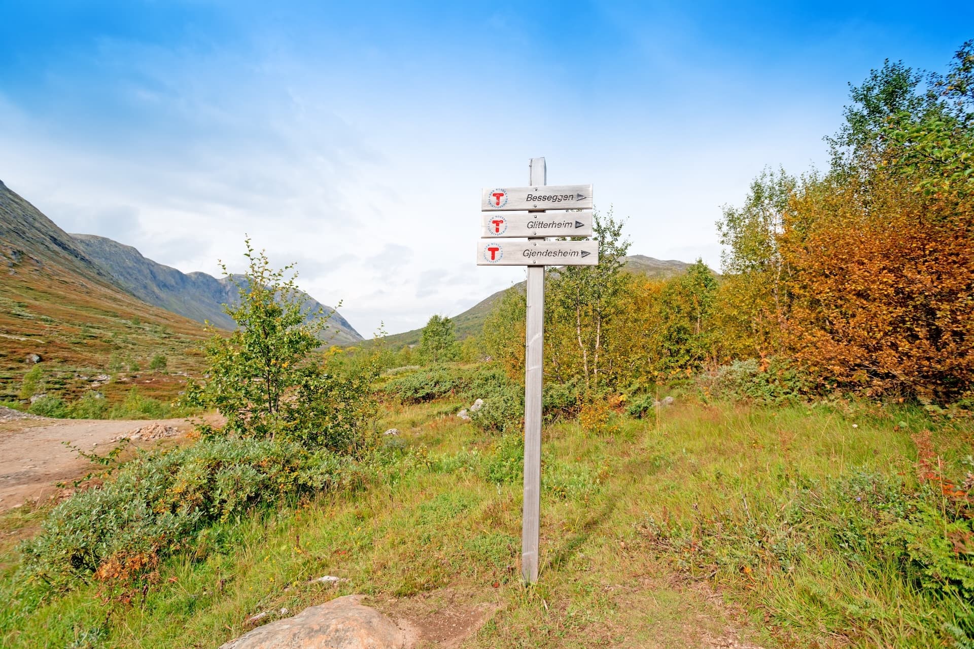 Hiking signpost pointing to Besseggen, Glitterheim, and Gjendesheim in a mountain valley.