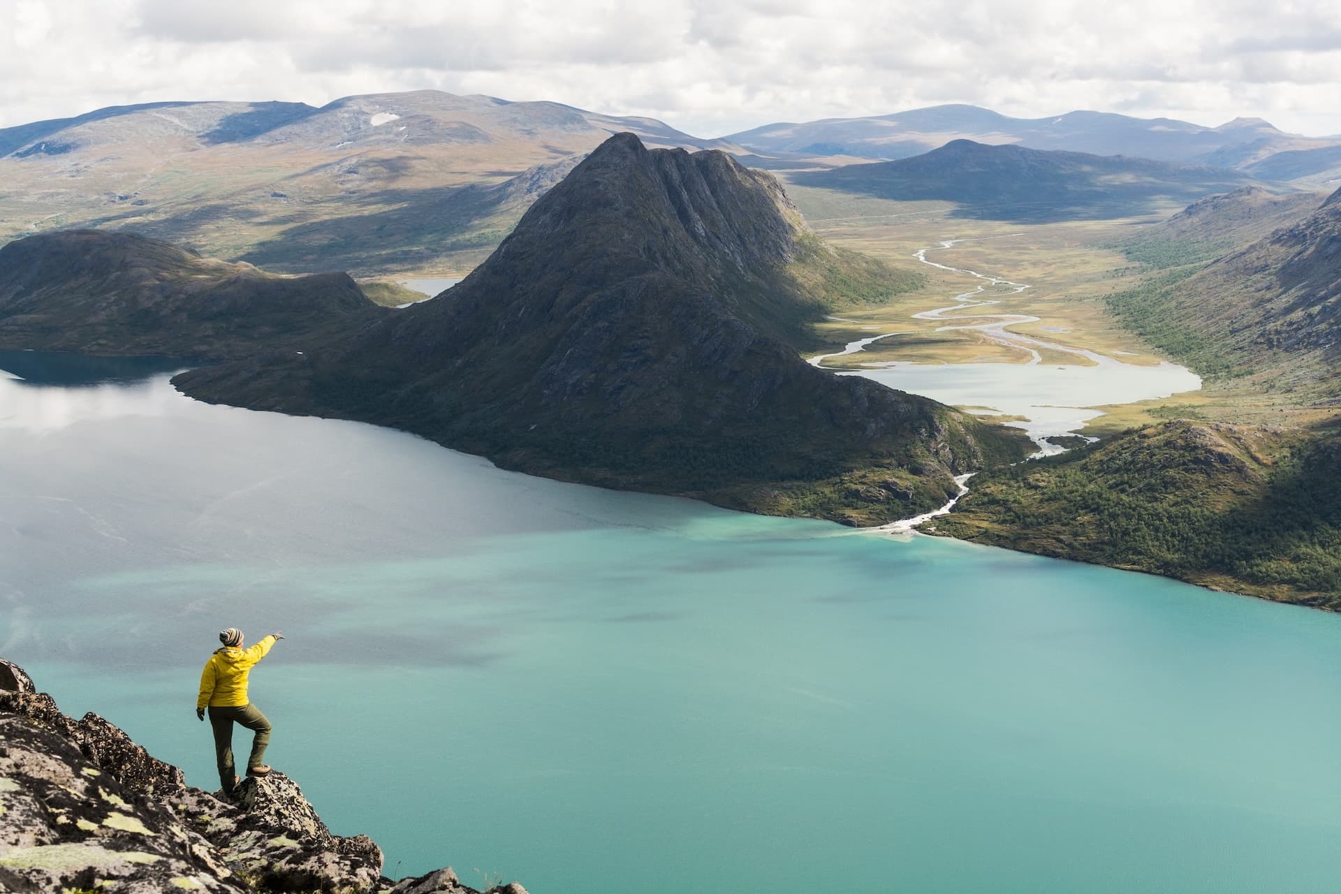 Hiker on Besseggen ridge pointing over turquoise lake and mountains in Norway.