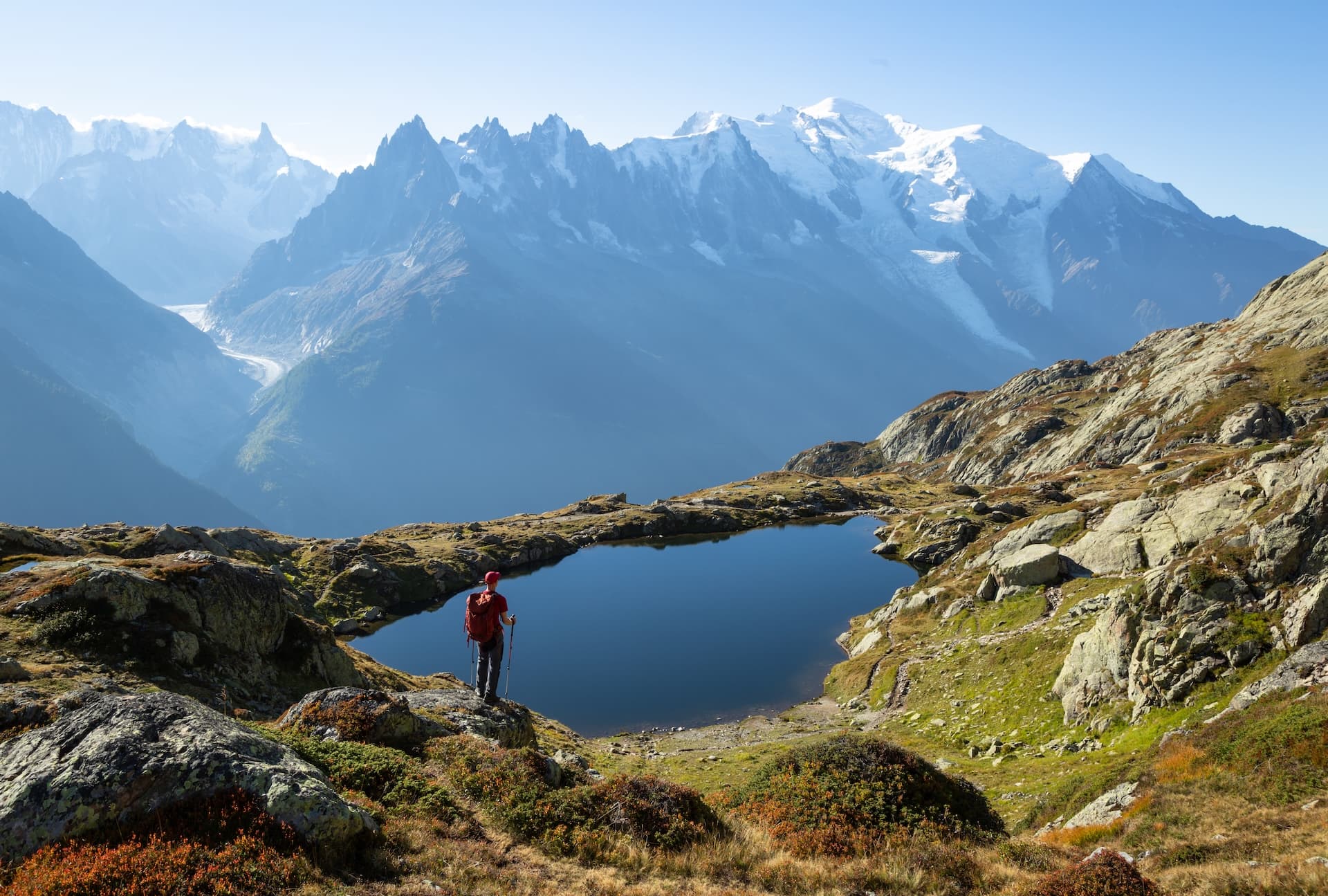 Hiker overlooking dark alpine lake with massive snow-capped mountains in the background