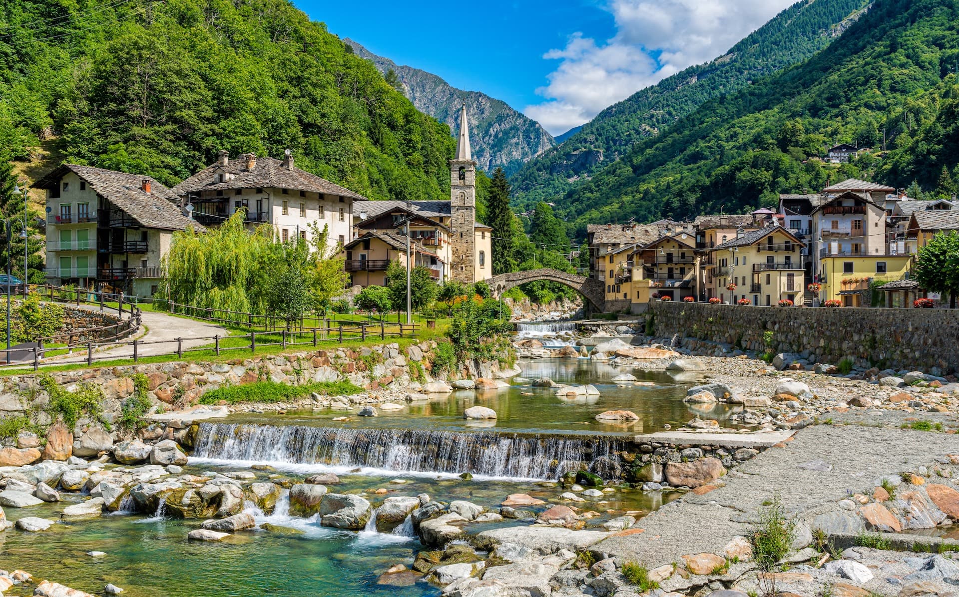 Alpine village of Courmayeur with stone church, river, and forested mountains.