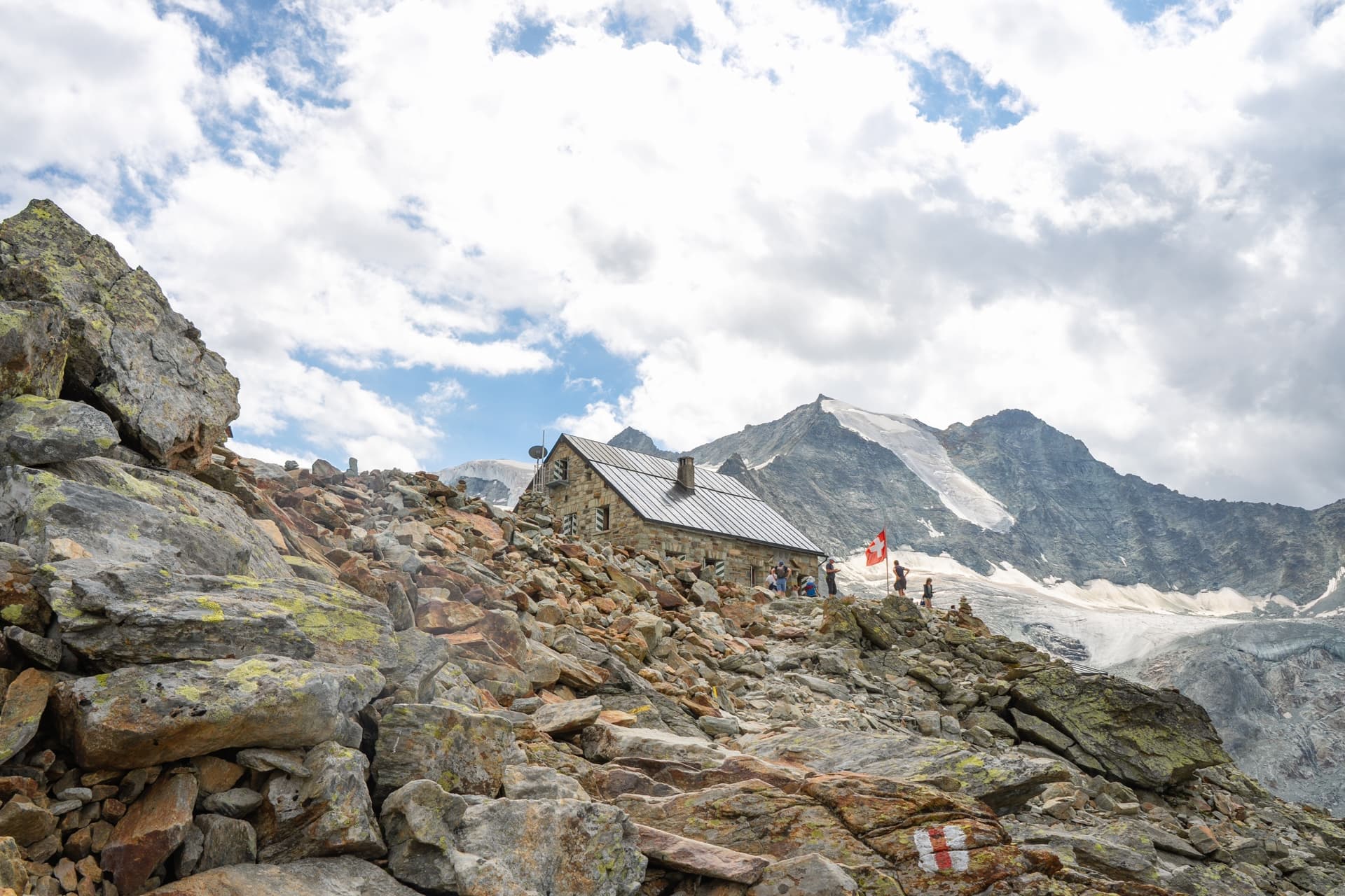 Stone mountain hut on rocky terrain near glacier, Swiss flag visible