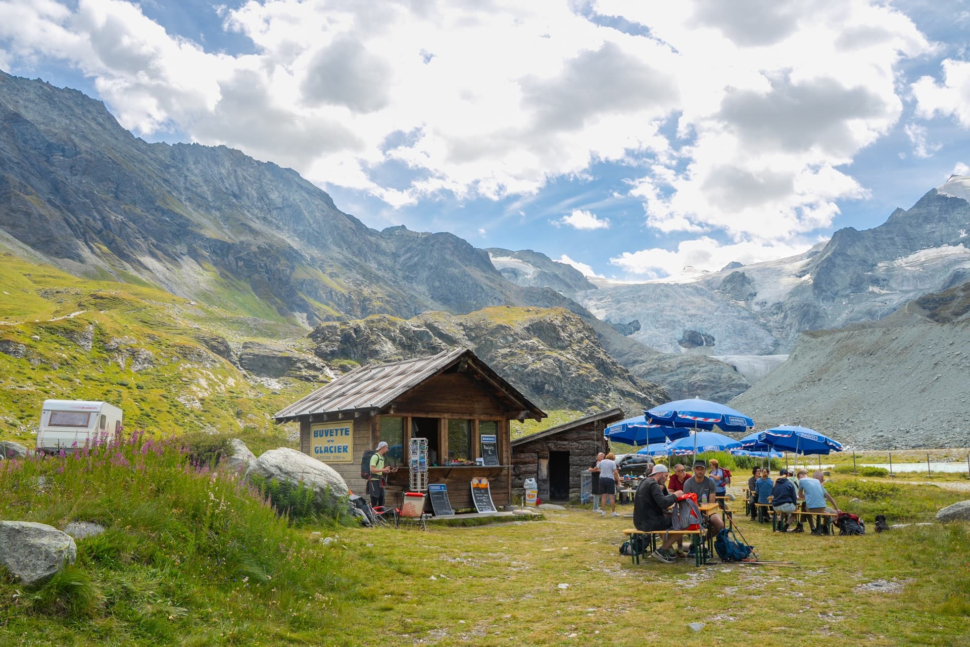 Hikers resting at Buvette du Glacier near Lac de Moiry with massive glacier and mountains.