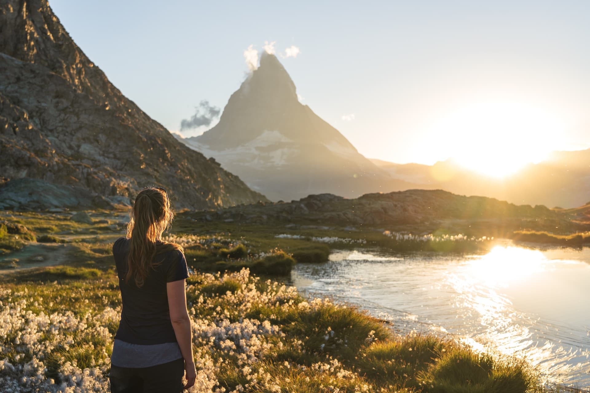 Hiker viewing Matterhorn reflection at Riffelsee lake during sunset with sun glare