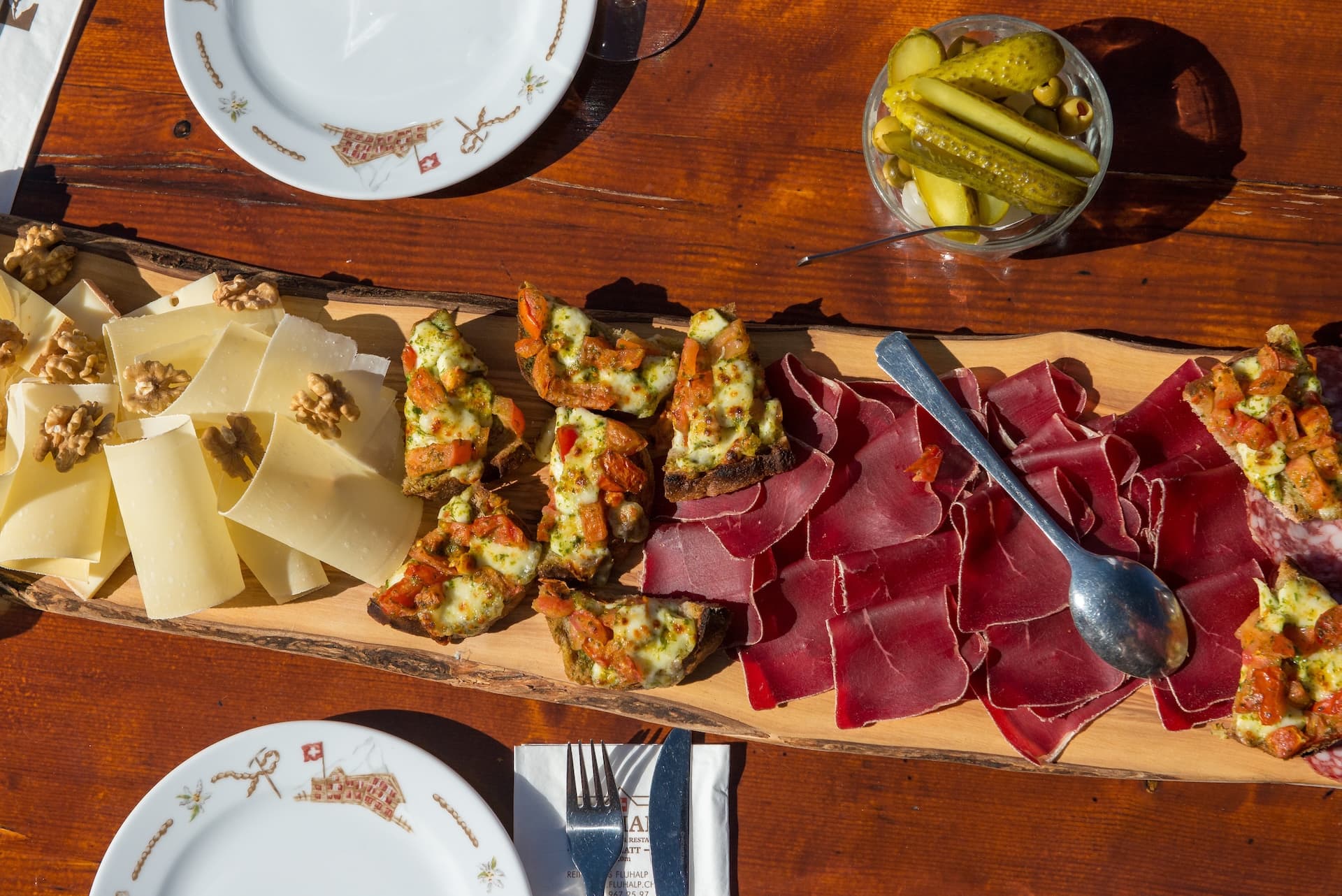 Charcuterie board with cheese, bruschetta, dried meat, walnuts, and pickles on a wooden table in Switzerland.
