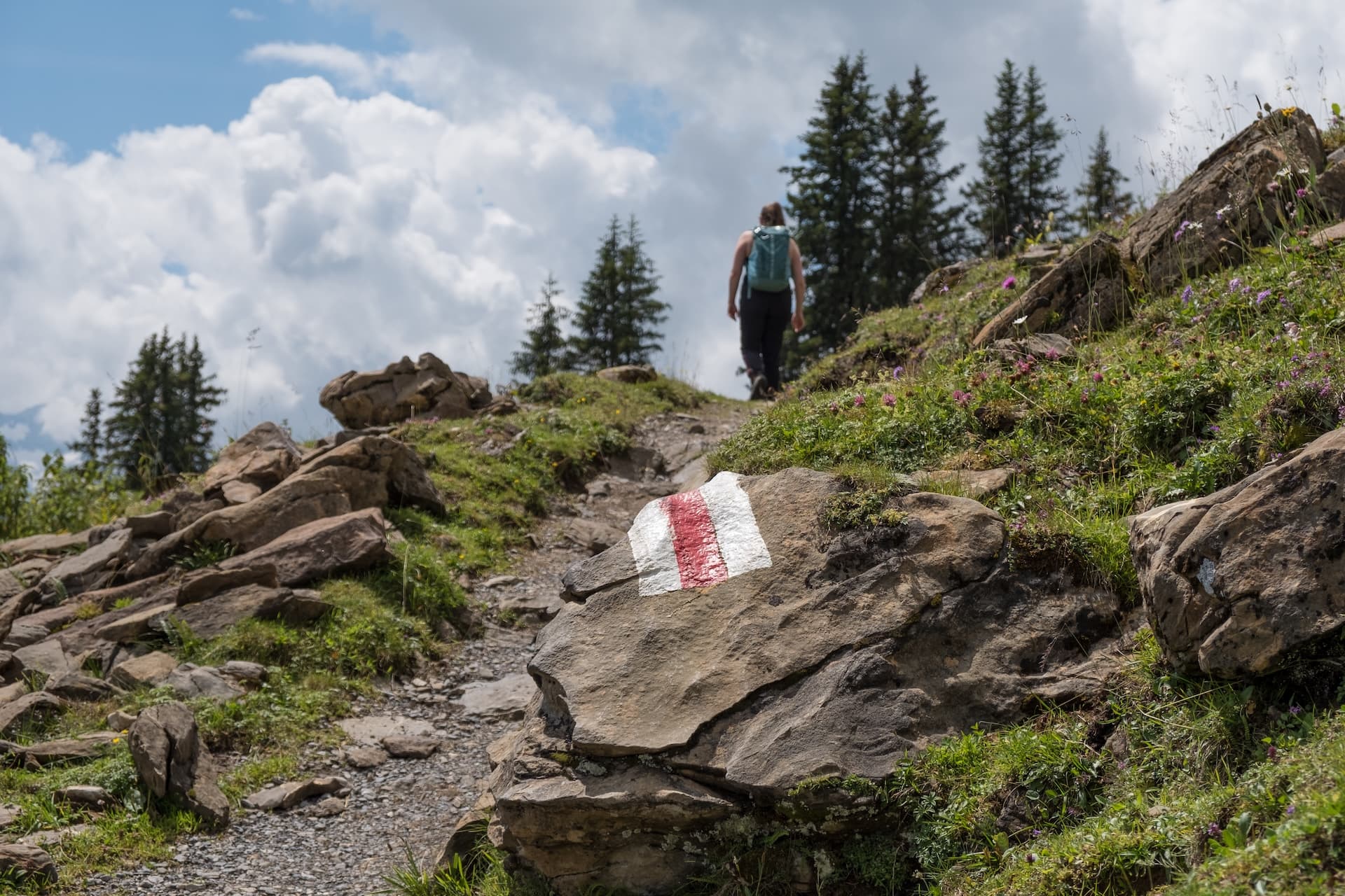 Hiking on a rocky mountain trail marked with a red and white blaze in Switzerland.