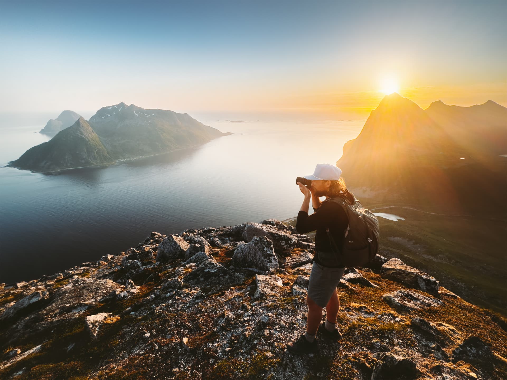 Photographer hiking on rocky peak taking pictures of mountains and sea at sunset in the Azores.