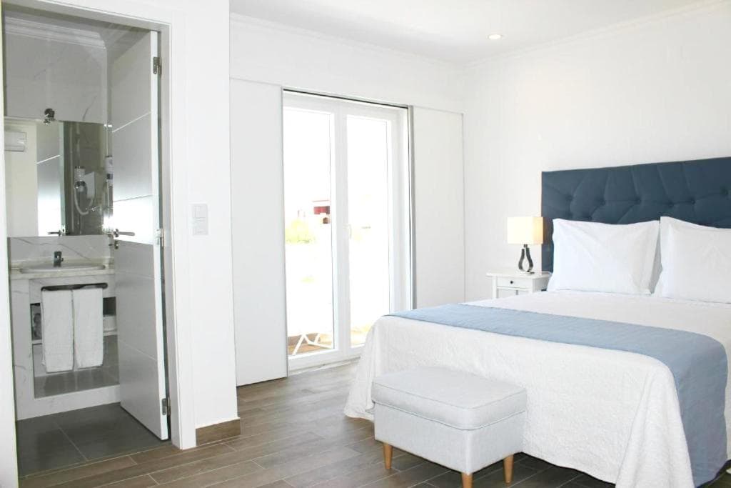 Bright hotel room with white bedding, blue headboard, and open bathroom entrance.