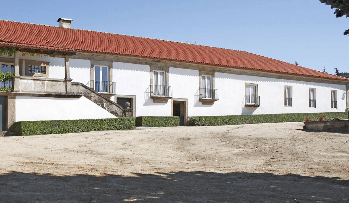 White stucco building with red tile roof, stone trim, and small Juliet balconies under clear blue sky.
