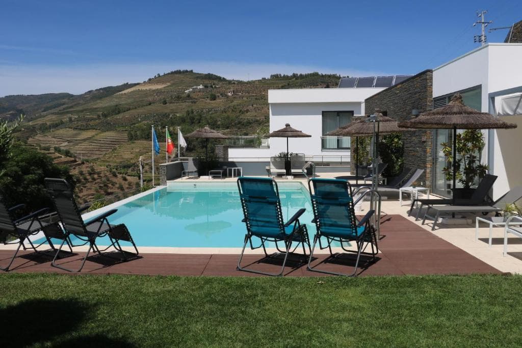 Infinity pool with lounge chairs overlooking terraced hillsides under a clear blue sky.