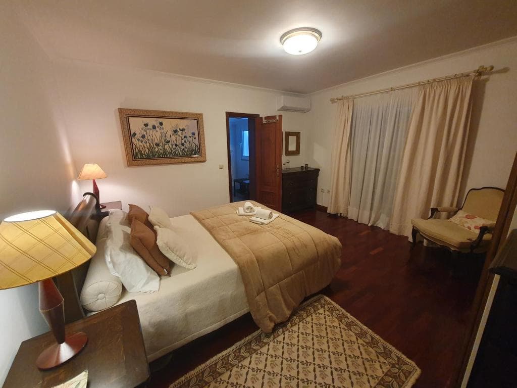 Bedroom with large bed, bedside lamps, dark wood floor, and floral artwork.