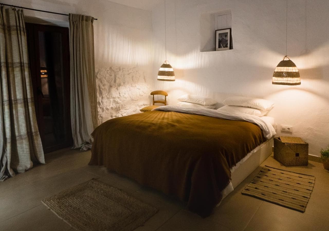 Cozy bedroom with white textured walls, brown bedding, and woven pendant lights in Casa De Los Cuadros