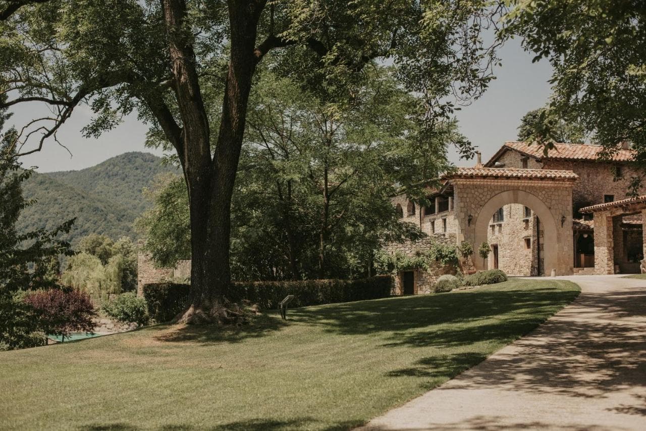 Stone Hotel El Mariner entrance with large tree and green mountains in background