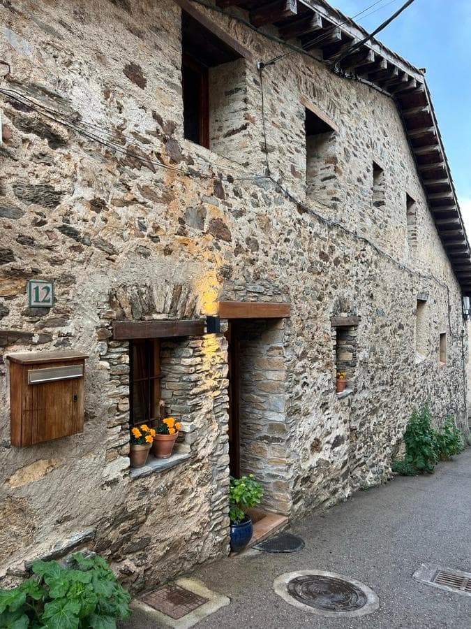 Stone building facade with number 12, wooden mailbox, and potted flowers on a narrow street, Casa Tapiolas Rectoría.