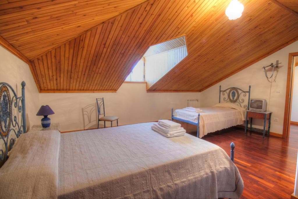 Guest house attic bedroom with wood ceiling, two beds, and hardwood floor in Casa do Destro.