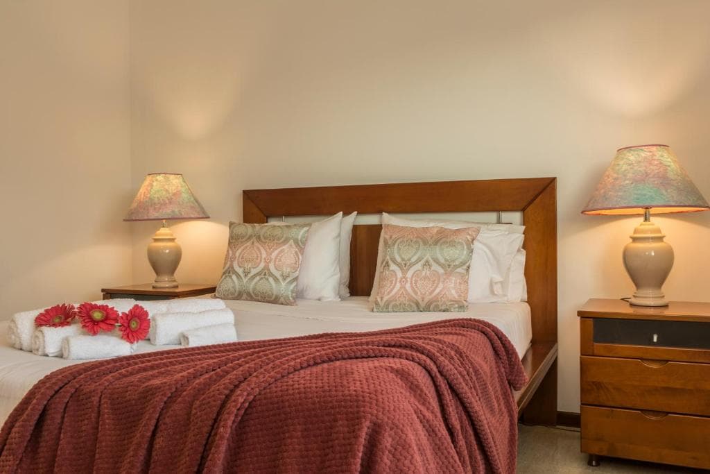 Bedroom with wooden bed frame, patterned pillows, red throw, and matching bedside lamps.