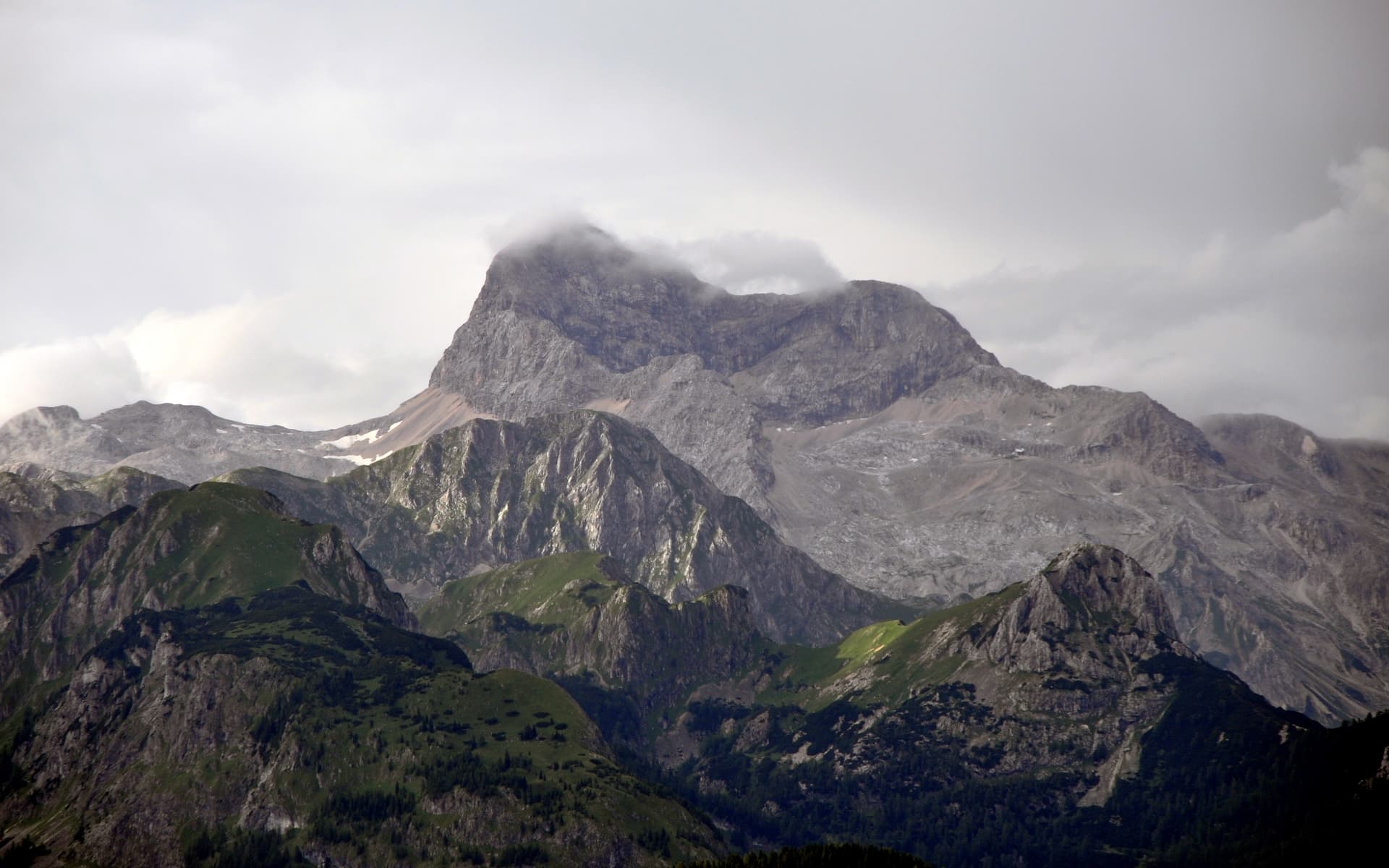 Rugged mountains with green lower slopes and rocky peaks shrouded in low clouds, likely Triglav National Park.