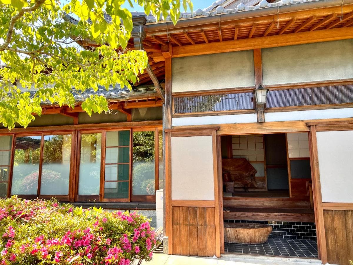 Entrance to NONAGASE GUEST HOUSE with bright pink flowers and traditional wooden architecture.