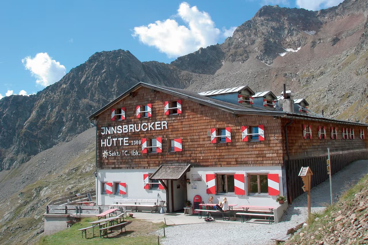 Innsbrucker Hütte mountain hut with red and white shutters at the base of rocky Alpine peaks.