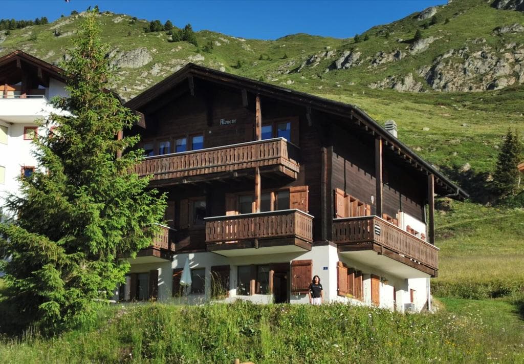 Wooden chalet in Riederalp against a green, rocky mountainside under a blue sky.