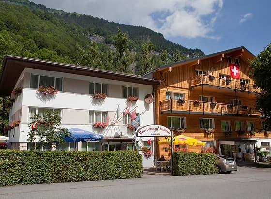 Hotel Gemse restaurant with outdoor seating and Swiss flag against a backdrop of green mountains.