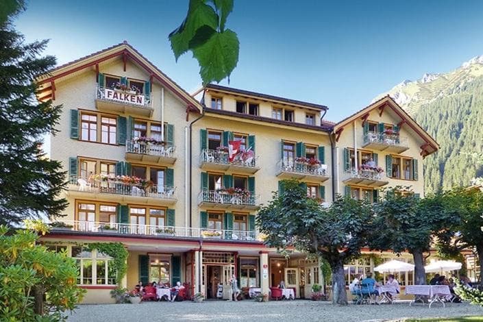 Hotel Falken building with balconies, outdoor dining, and mountain backdrop.