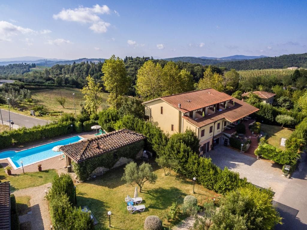 Yellow villa with swimming pool surrounded by lush greenery and rolling hills under blue sky.