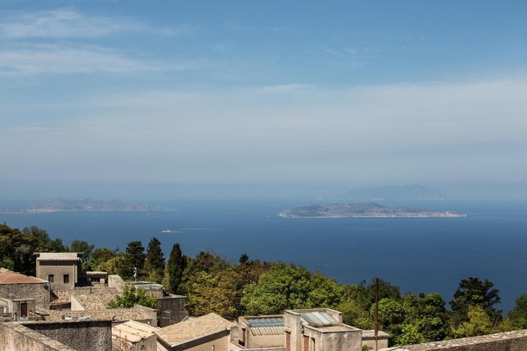 Coastal town rooftops overlooking the blue sea with distant islands under a bright sky.