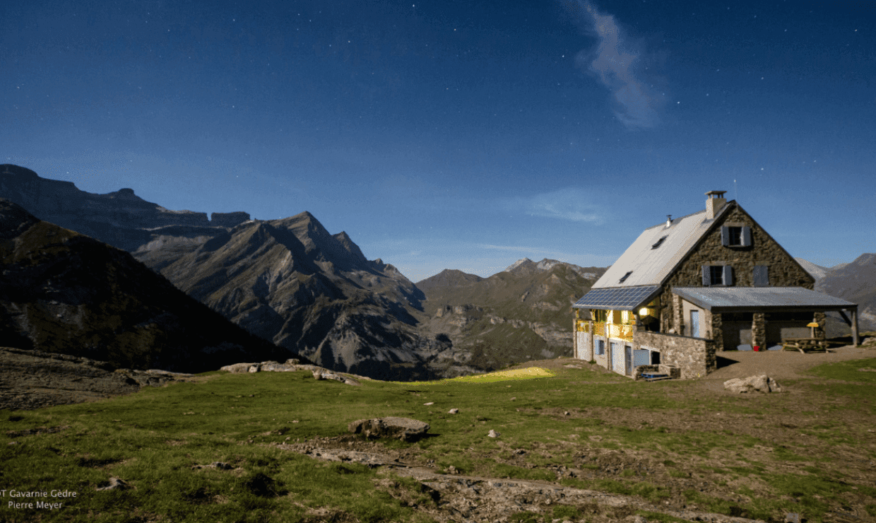 Refuge de Espuguettes stone hut illuminated at night with starry sky and Pyrenees mountains.