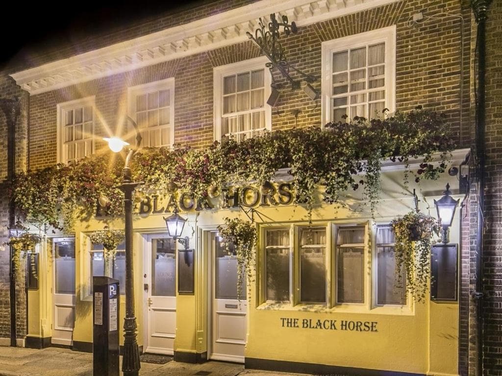 The Black Horse Inn exterior at night, illuminated with hanging greenery and street lamps.