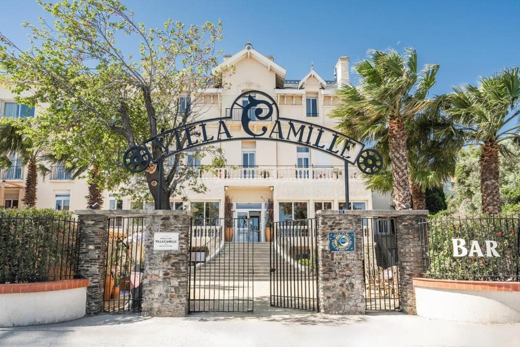 Villa Camille Hotel & Spa entrance with wrought iron sign, stone pillars, and palm trees.